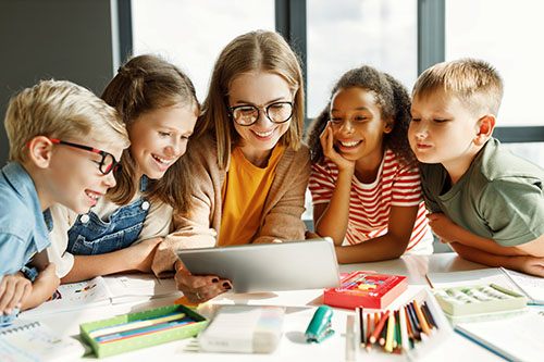 Happy,Female,Tutor,And,Optimistic,Children,Smiling,And,Watching,Video